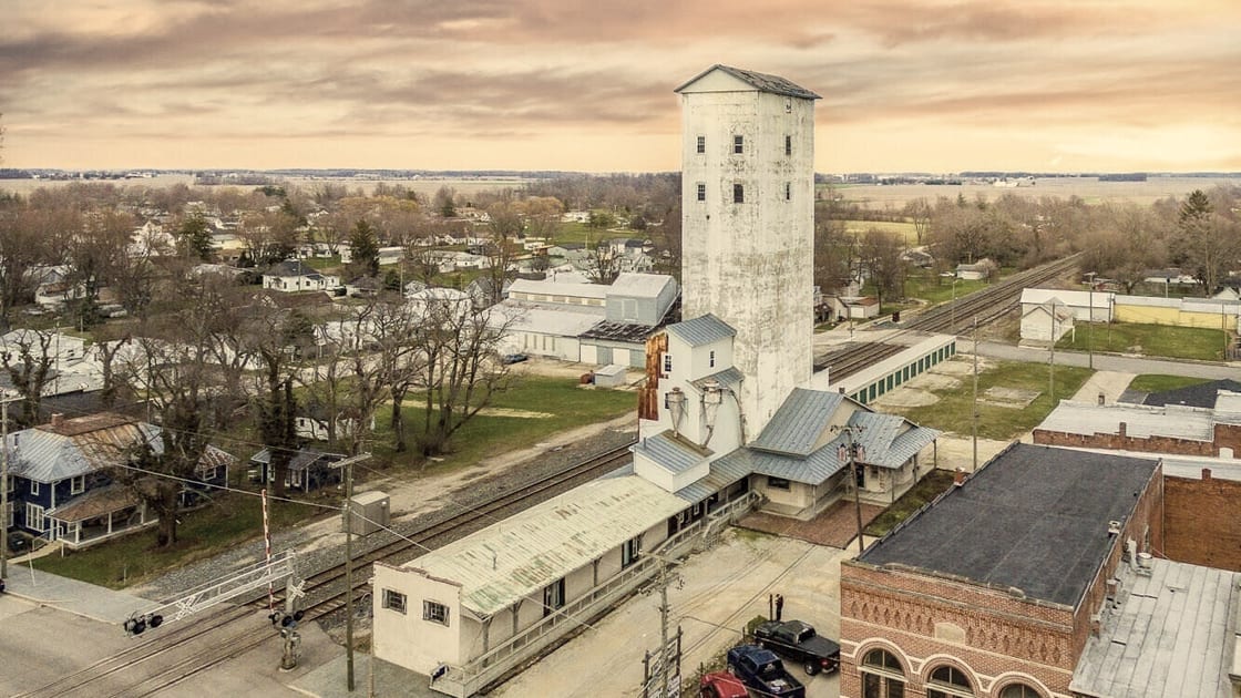 Aerial view of the Goodrich grain elevator tower rising above Farmland, Indiana at sunset